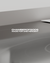 A minimalist design featuring the text 'CHAMBEROFGODS' in bold, followed by 'MADE FOR ONE PERCENT' in a smaller font. The background is a smooth, gradient gray surface with subtle reflections, emphasizing a sleek and premium aesthetic.
